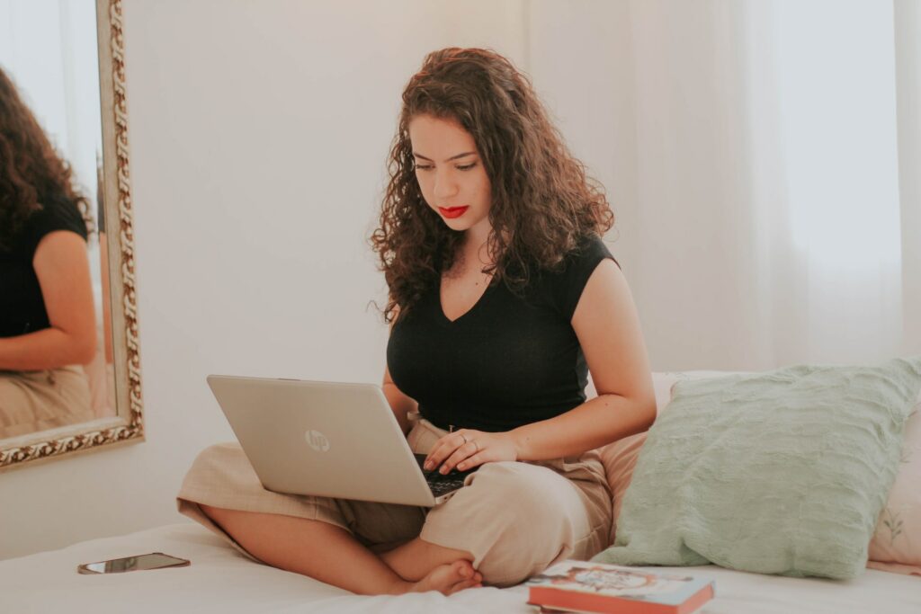 A person sat on their bed using a laptop searching for the best work from home routine. 